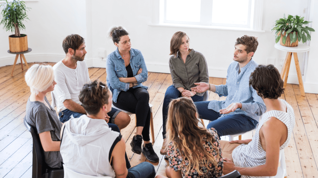 um grupo de 8 pessoas sentadas em cadeiras, em forma de círculo, conversando