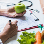 nutricionista segurando uma maçã e escrevendo. uma cesta de salada compõe a cena