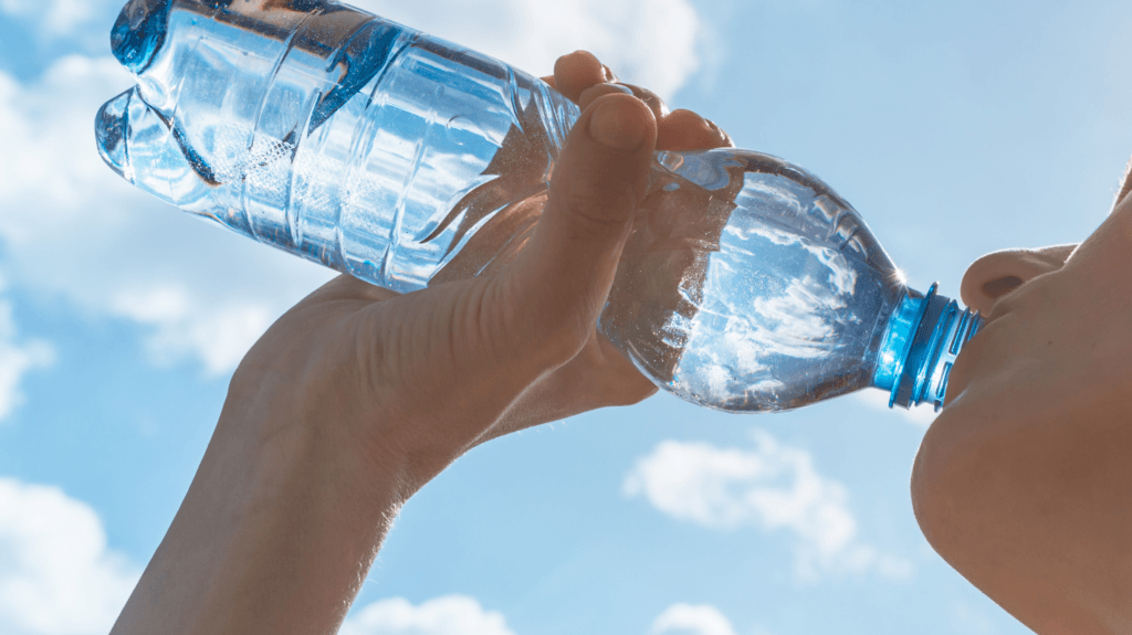 uma mulher bebendo uma garrafa de água com o céu ensolarado ao fundo