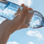 uma mulher bebendo uma garrafa de água com o céu ensolarado ao fundo