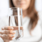 uma mulher, desfocada ao fundo, segurando um copo de água