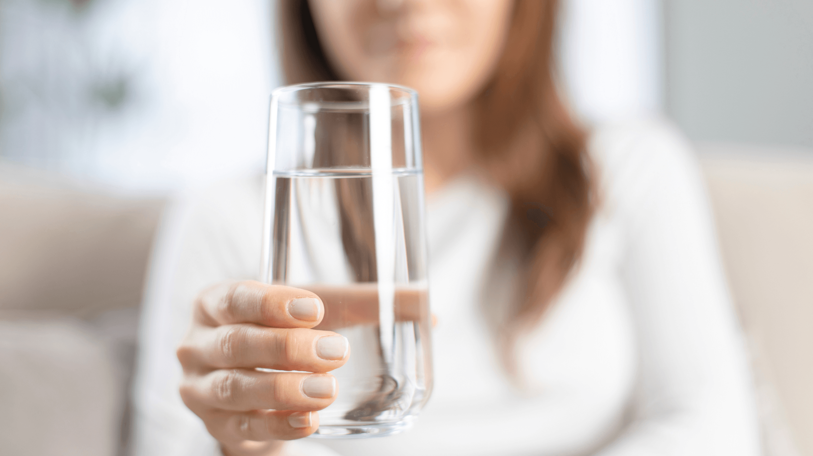 uma mulher, desfocada ao fundo, segurando um copo de água